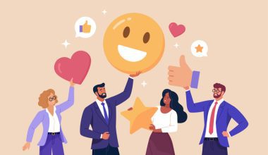 Four business professionals standing together holding large icons representing positive feedback, including a smiling emoji, a heart, a star, and a thumbs-up symbol, with speech bubbles showing likes and ratings.